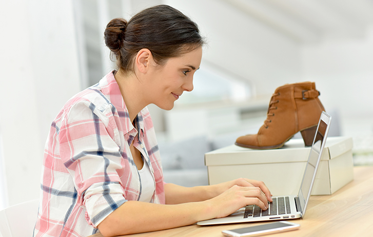 person typing on their laptop with a shoe on a box beside them