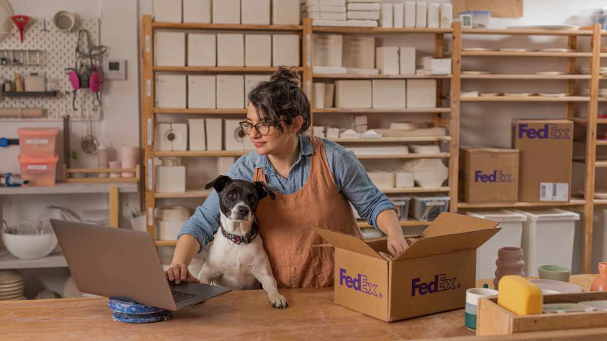 a woman browsing the computer and packing a box with her dog by her side