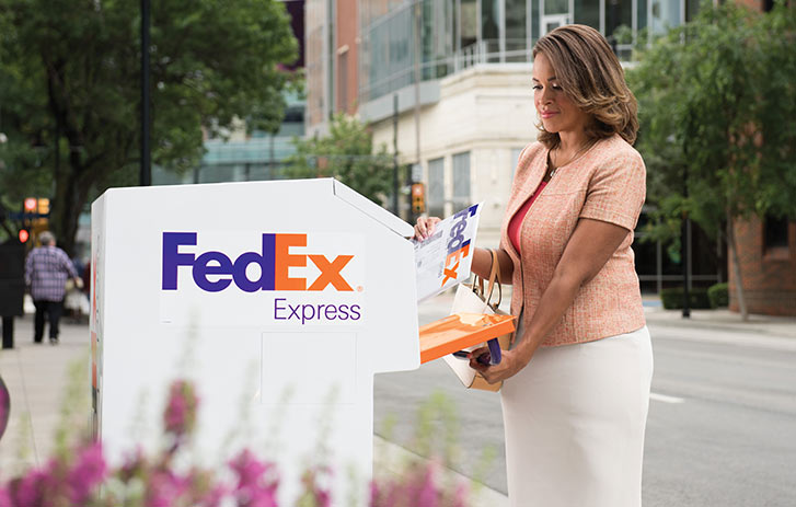 A woman dropping off a fedex box into a dropbox location