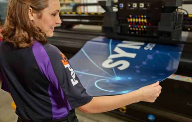 Smiling FedEx Office team member working on banner at large printer