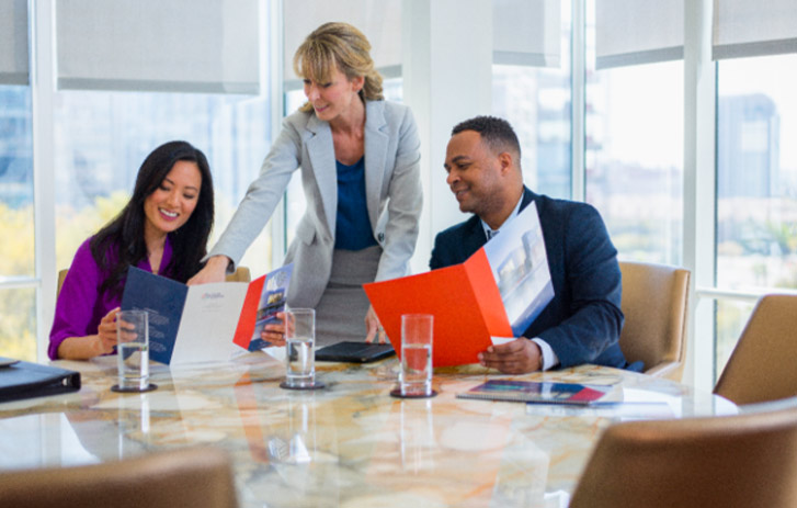 Three business professionals smiling and looking at tri-fold brochures and folders
