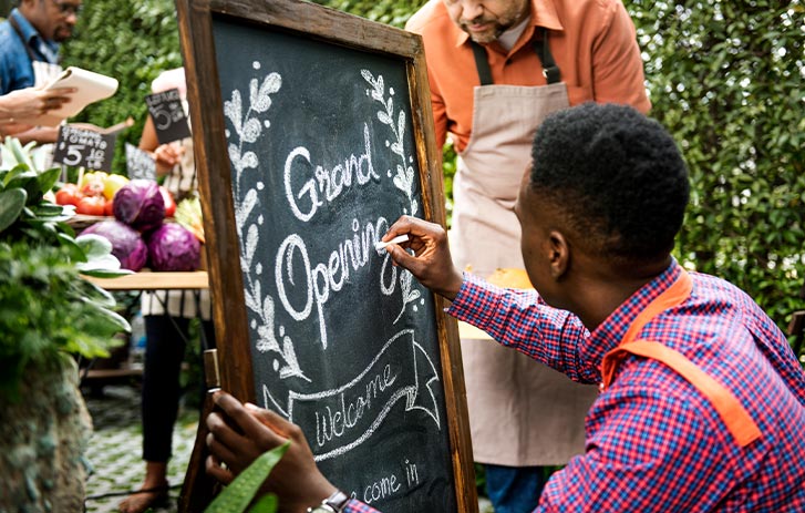 Shop owner writing open on framed chalkboard Shop owner writing open on framed chalkboard