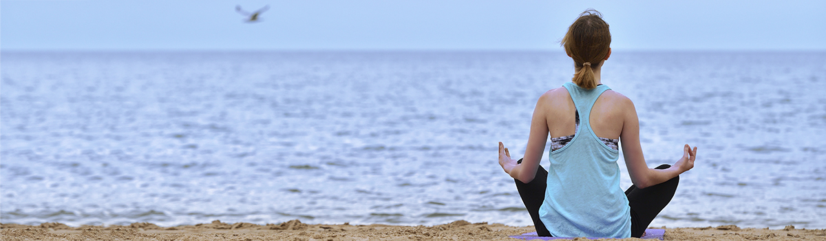Woman meditating on a sandy beach.