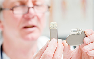 A doctor closely examines a pacemaker and an implantable cardiac monitor.