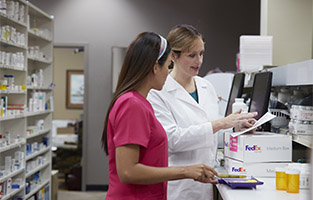 A pharmacy tech counts pills as a pharmacist prepares FedEx Express packages.