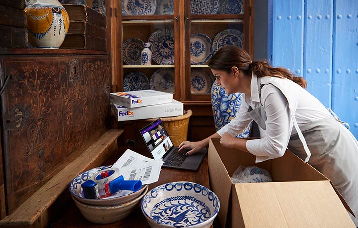 Small Business Center Fedex - a woman packs pottery for shipping and researches shipping on fedex com