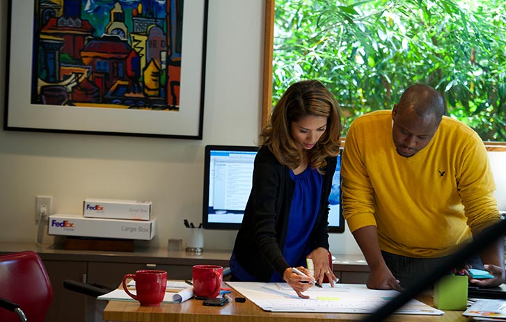 A photo of a man and a woman leaning over a desk, making notes on a large pad of paper.
