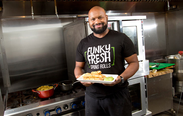 Funky Fresh Spring Rolls A photo of Funky Fresh Spring Rolls founder Trueman McGee holding a platter of rolls in a kitchen
