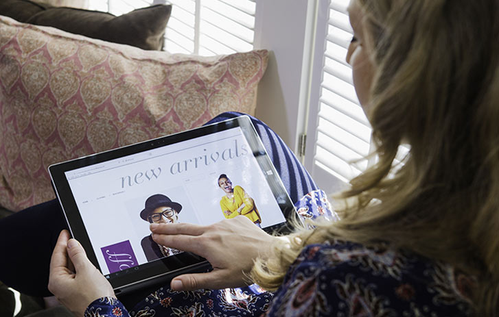 A photo of a woman shopping online while sitting on a sofa.