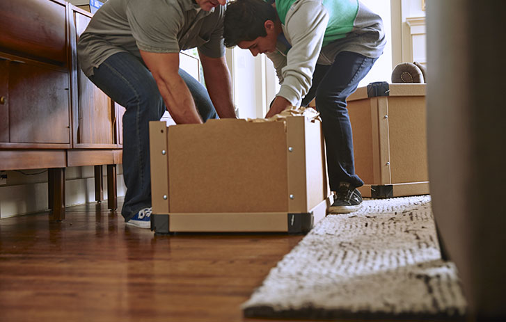 A photo of two people removing something from a box in a residential setting.