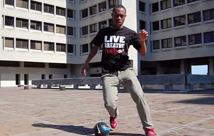 A photo of Ebun Olaloye from Live Breathe Futbol dribbling a soccer ball outside a building