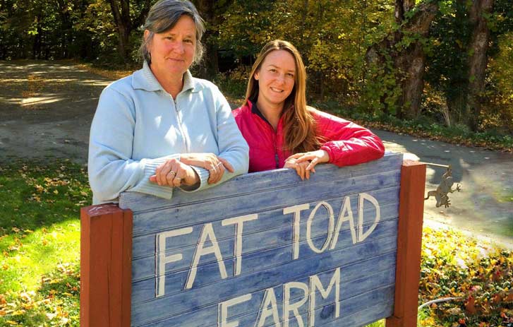 A photo of two women standing behind a Fat Toad Farm sign
