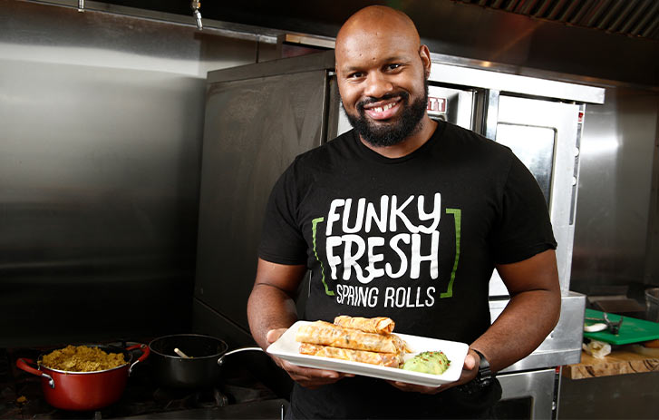 Funky Fresh Spring Rolls A photo of Funky Fresh Spring Rolls founder Trueman McGee holding a platter of rolls in a kitchen