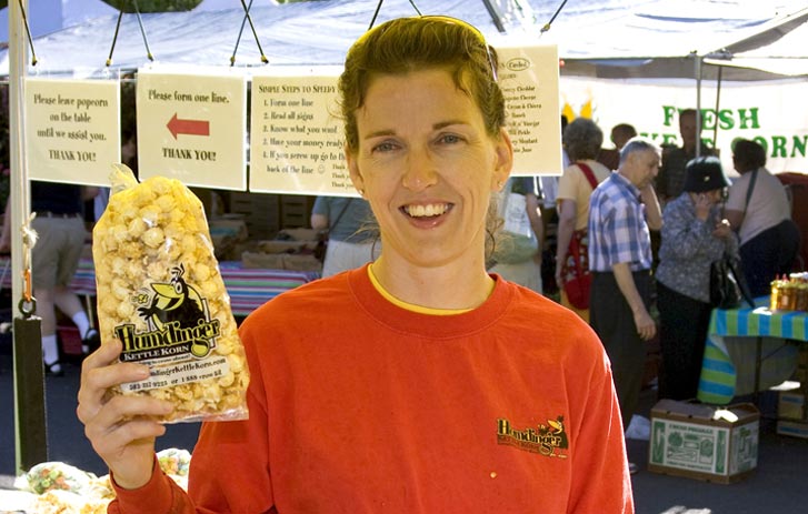 A photo of a woman holding a bag of Humdinger Kettle Korn at a festival