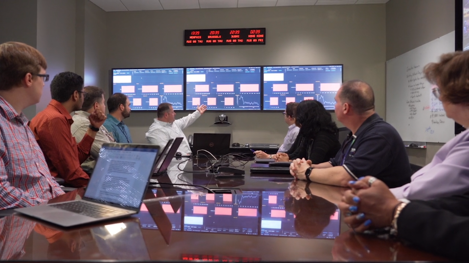 Multiple people sitting around a table looking at TV monitors