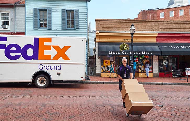 A FedEx team member uses a dolly to bring packages across the street.