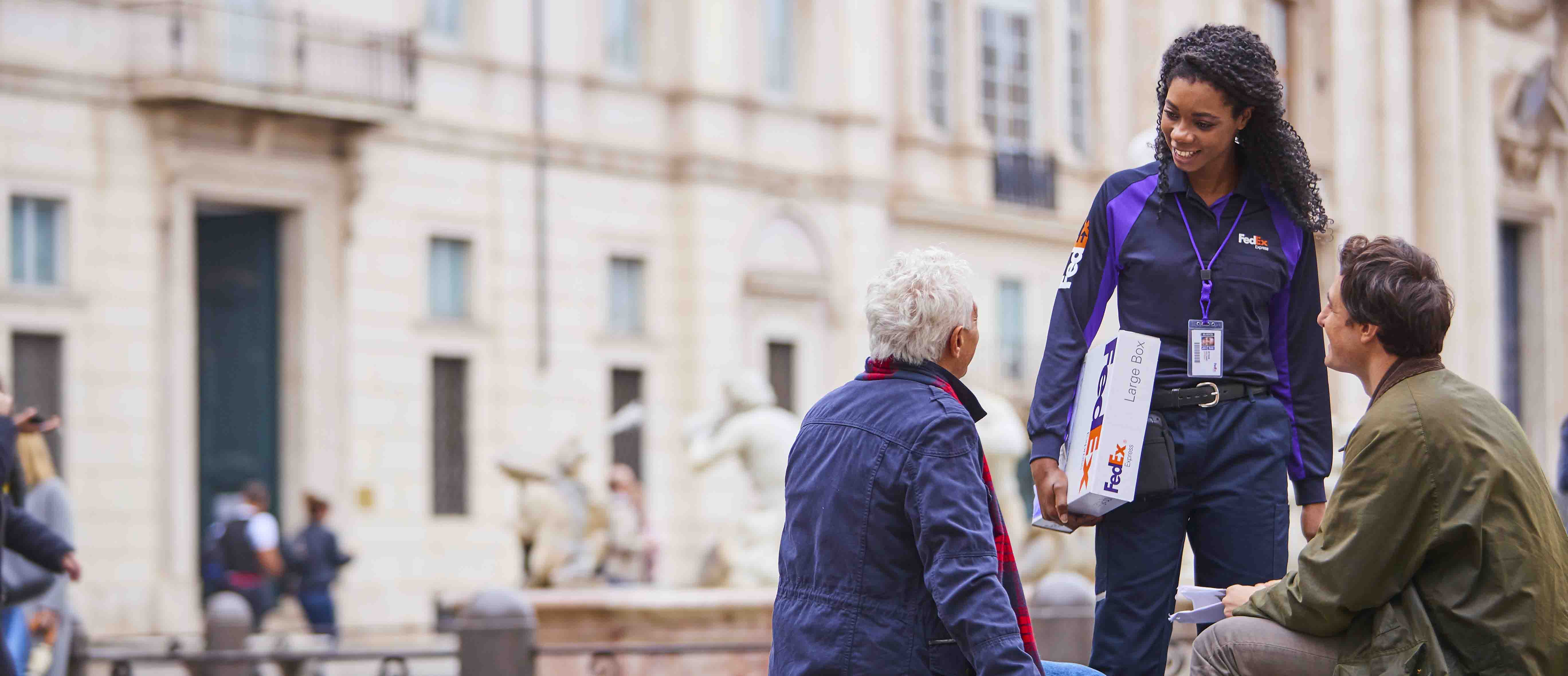 Two people sitting talking to a FedEx courier.
