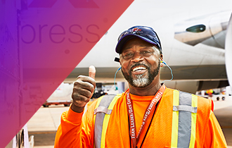 Team member by a FedEx airplane, giving a thumbs up.