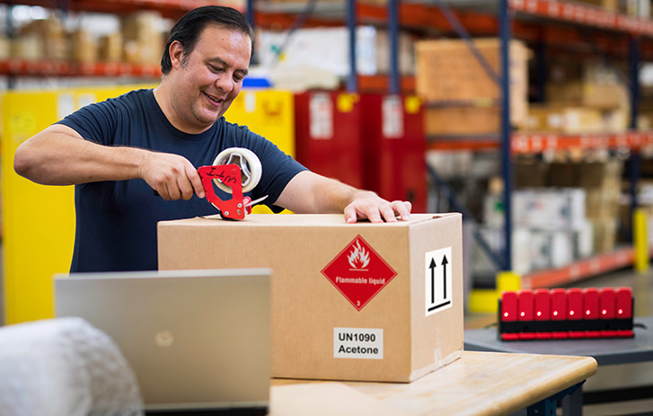 A man taping a box with a hazardous material label on it.