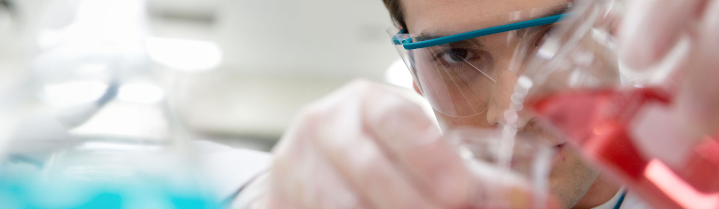 Man pours reddish liquid into container in lab