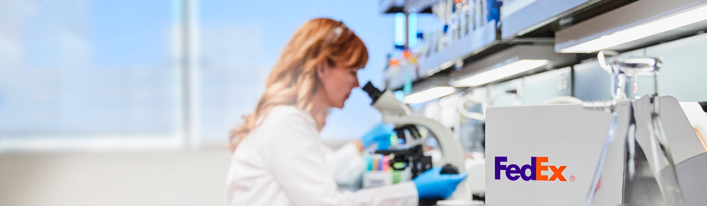 Lab tech looks into microscope with FedEx box on counter