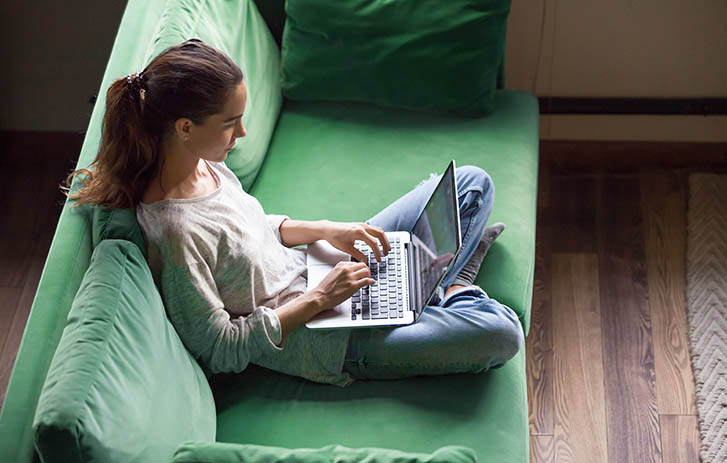 Person sitting on a green sofa using their laptop computer