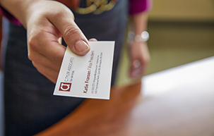 Closeup of a hand holding a business card as if passing to the person holding the camera.