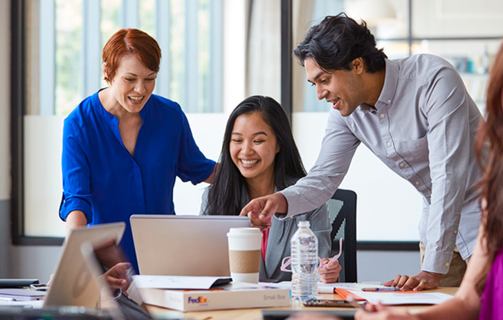 Two women and a man looking at a laptop screen at a conference table with a FedEx small box sitting on the table.
