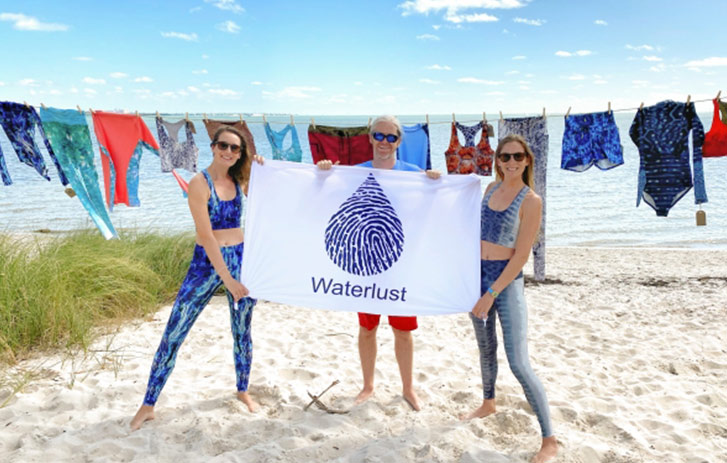 women on beach holding waterlust sign