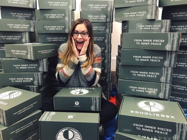 Julia, co-founder of BroglieBox, poses in front of hundreds of mental health care packages.