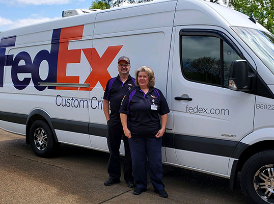 Sammy y Martha Garner de pie junto a su vehículo de FedEx Custom Critical