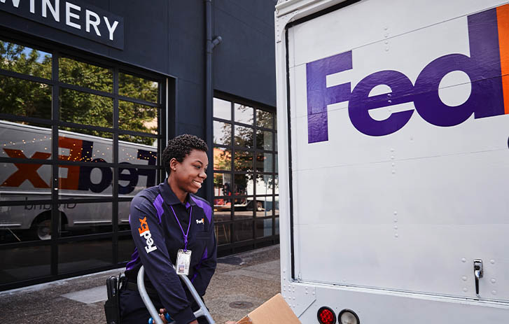 A FedEx team member pushing a dolly in front of a FedEx truck.