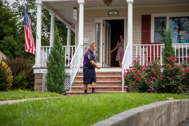 FedEx delivery driver waiving at woman picking up a package at the door