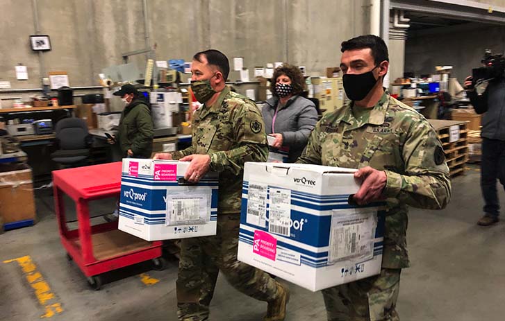 Two people in army fatigues carrying boxes.