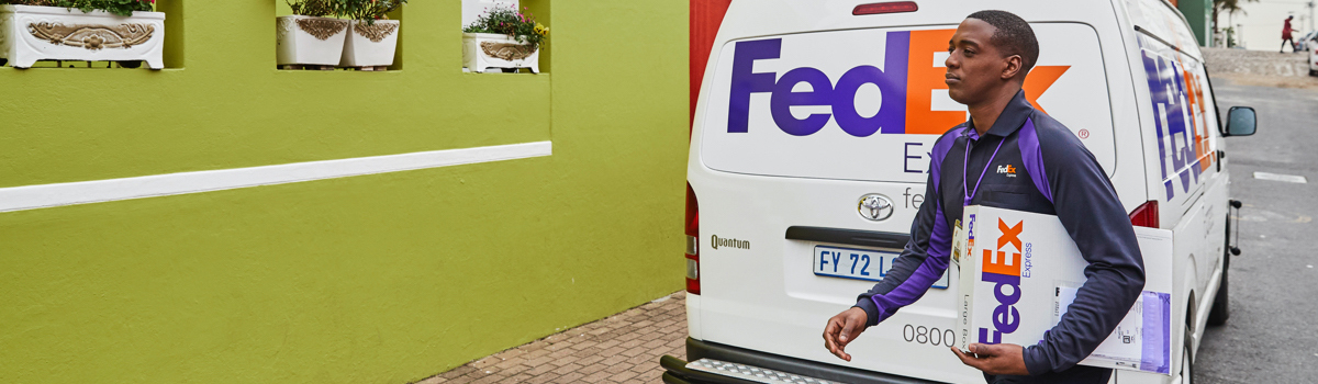 A FedEx Express courier carrying a package with a FedEx Express truck in the background