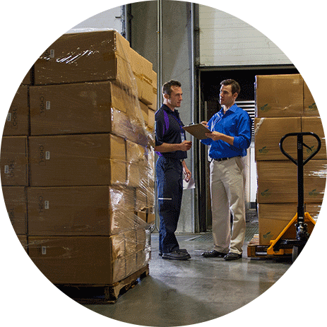 Warehouse worker talking to a FedEx truck driver surrounded by freight pallets