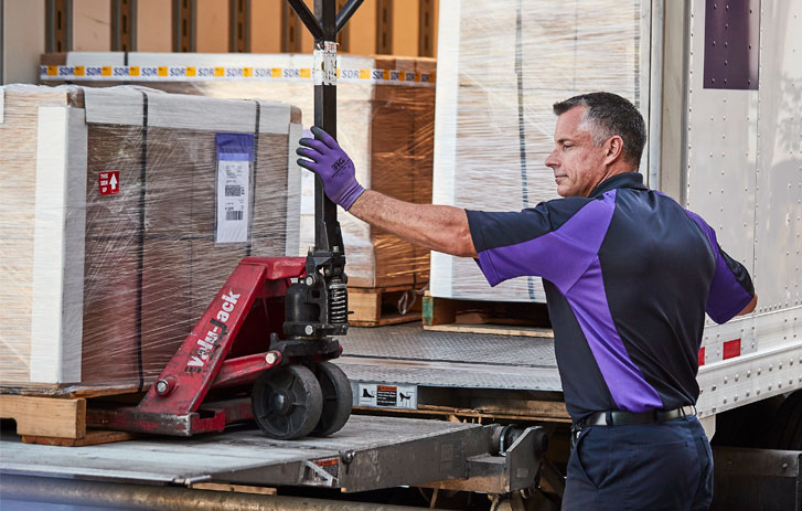 A FedEx driver loading freight onto a semi-truck liftgate