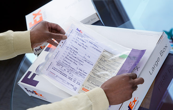 A person affixing a label to a FedEx white shipping box