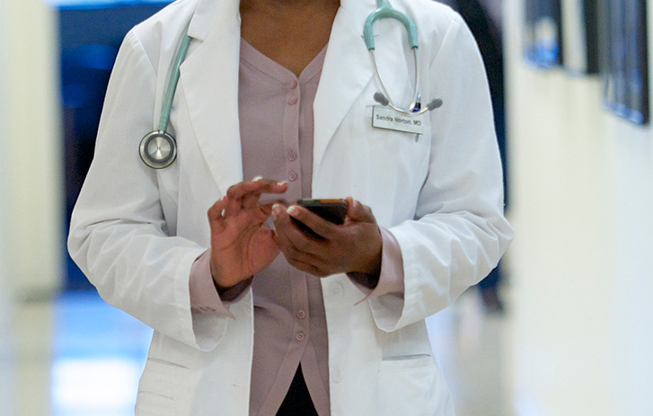 A close up view of a doctor using a smart phone while walking forward