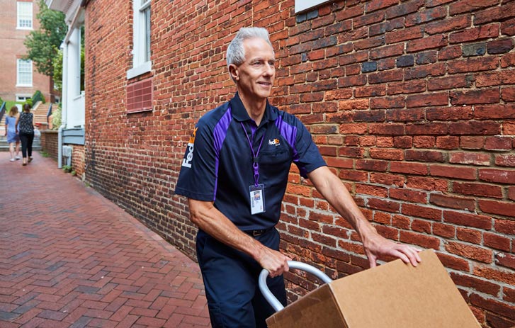 FedEx courier pushing large package on moving dolly