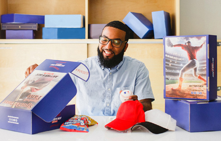 Man with custom branded boxes looking in a box and holding a hat.