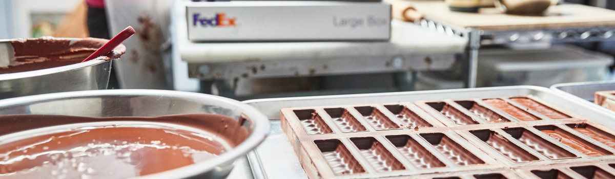 Melted chocolate in a bowl on a metal counter with FedEx packages in the background.