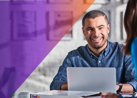 Man sitting behind a laptop smiling at another person