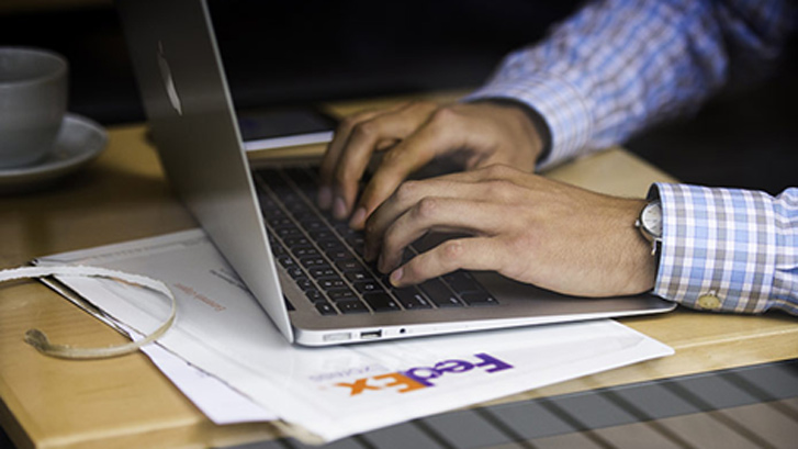 hombre escribiendo en una computadora portátil con un fedEx Envelope en una mesa cerca de él