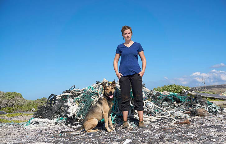 Kat Crabill, founder of Nurdle in the Rough, standing with her dog in front of pile of materials